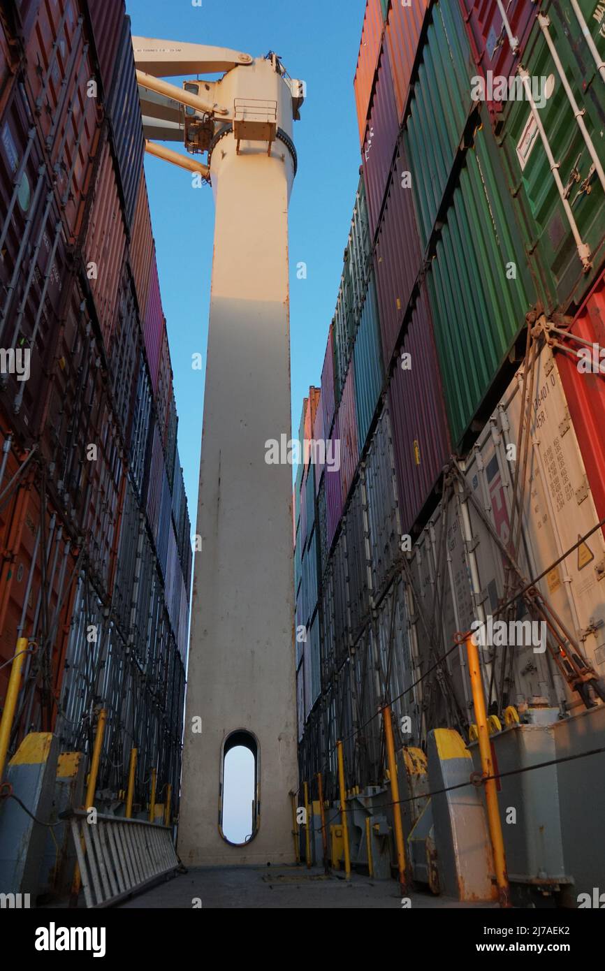 Cream color cargo crane between containers lashed and secured with twist locks and lashing bars  on container vessel sailing through sea. Stock Photo