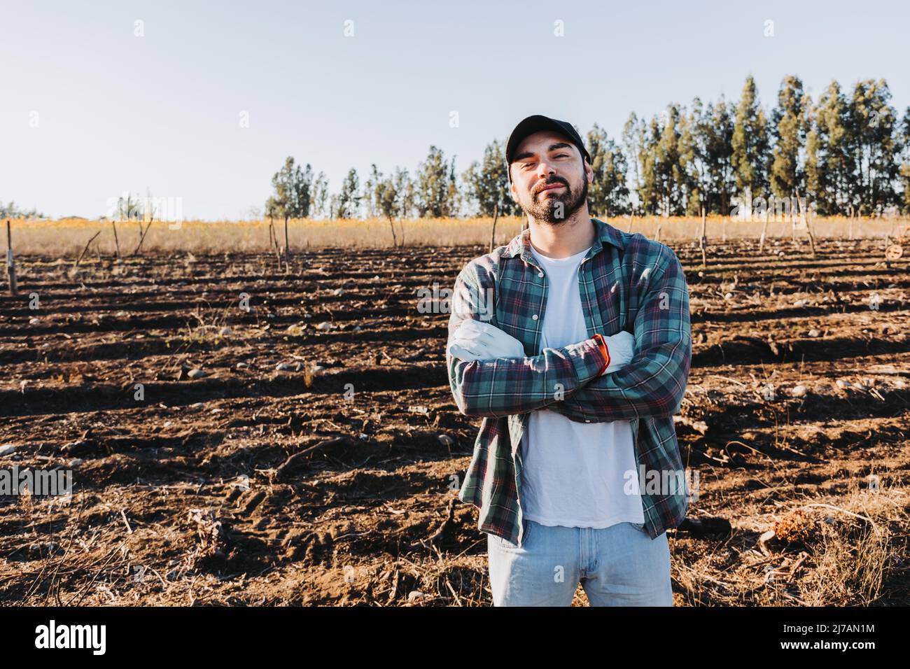 Young latin farmer man with crossed arms in the middle of the farmland. Agricultural sustainability concept. Stock Photo