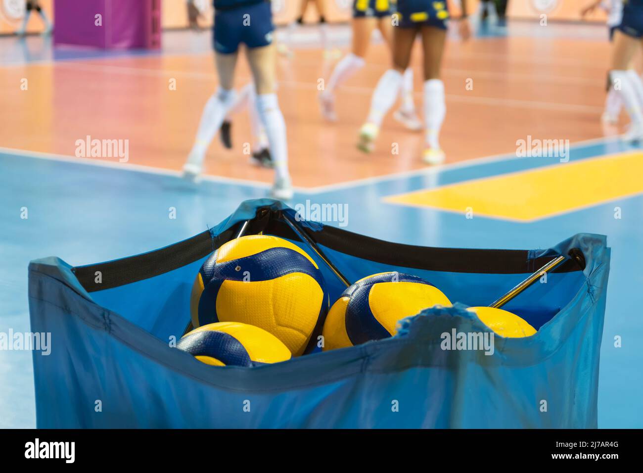 Volleyball balls are in a cloth box and in the background professional