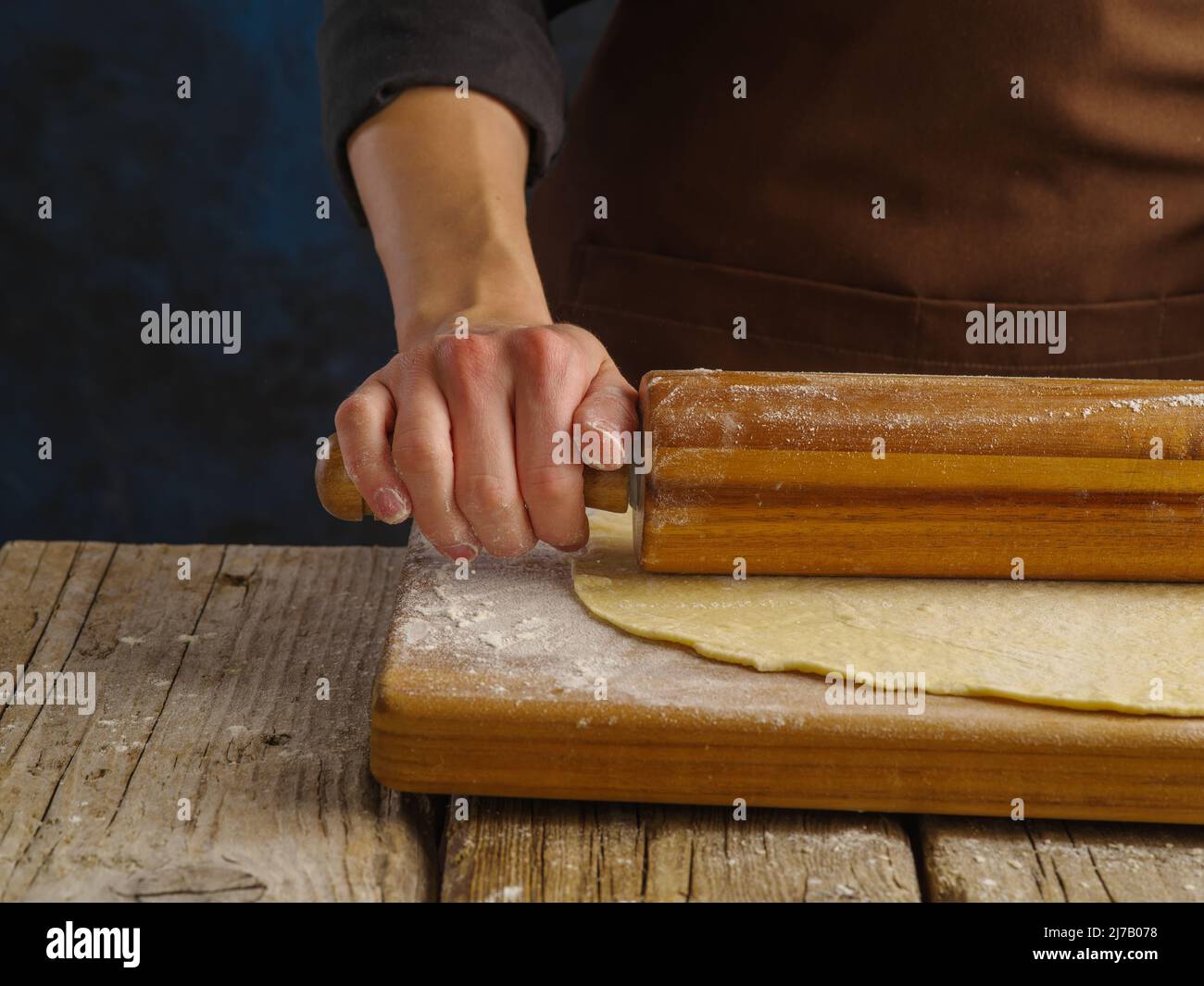 Macro shot. The chef rolls out the dough with a rolling pin on a wooden background. The concept is recipes for dough products - pastries, pasta, pizza Stock Photo