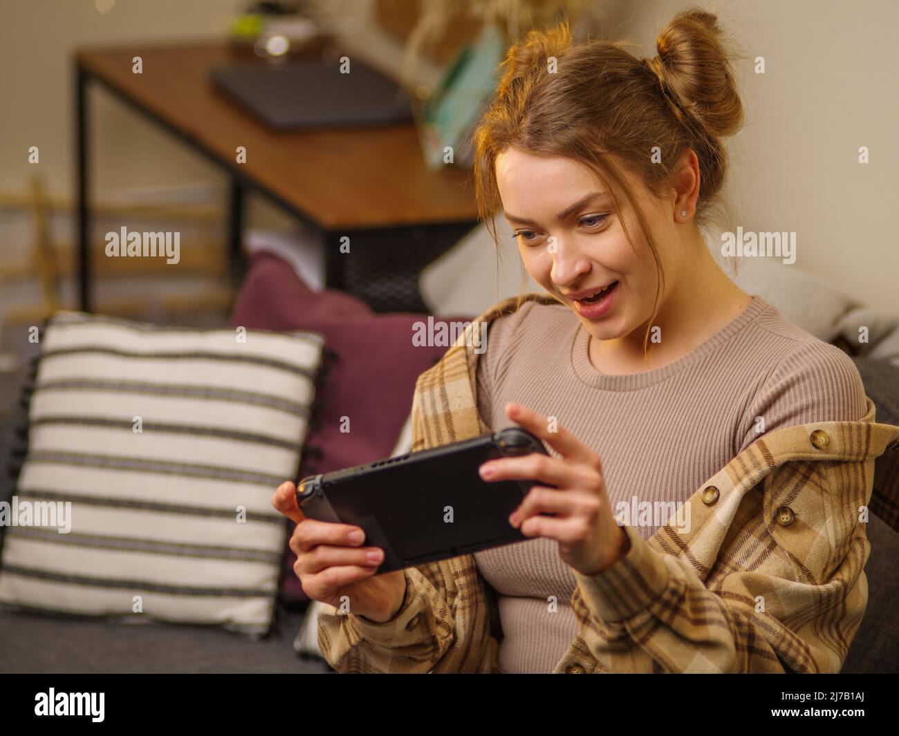 A girl with a portable game console enthusiastically plays a video game. The background is the interior of the room. Electronics, communication, leisu Stock Photo