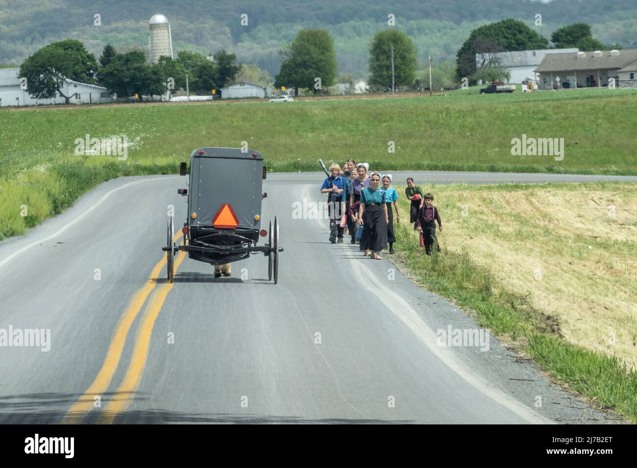 Lancaster County, Pennsylvania-May 5, 2022: Group of Amish women and children walking on rural road wave to a passing horse and buggy. Stock Photo