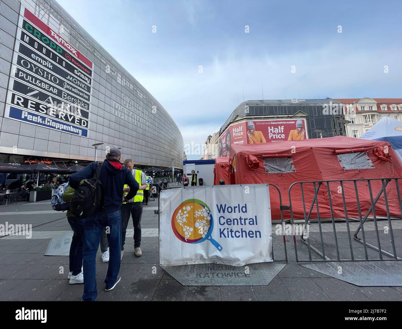 May 7, 2022, Katowica, Poland: Ukrainian refugees talks to a yellow vested  security volunteer in front of World Central Kitchen Tent, outside the  Katowice train station, which a music video plays on