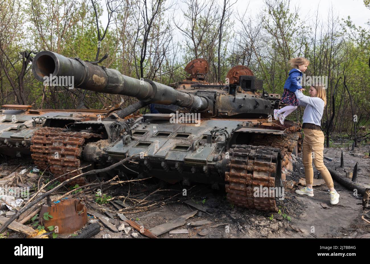 A mother lifts her daughter on the tower of a destroyed Russian tank near Makariv village, Kyiv region. Russia invaded Ukraine on 24 February 2022, triggering the largest military attack in Europe since World War II. Stock Photo