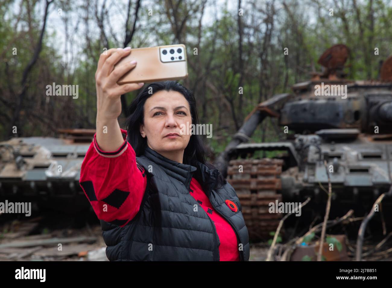 A woman takes a selfie in front of a destroyed Russian tank. Russia invaded Ukraine on 24 February 2022, triggering the largest military attack in Europe since World War II. Stock Photo