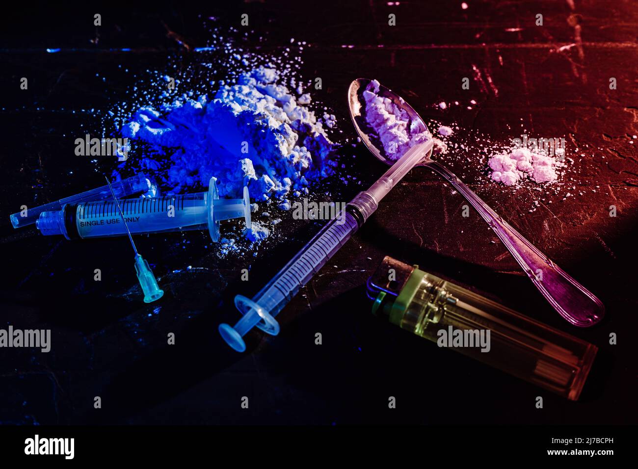 Syringes, spoon, drugs on a black, dimly lit surface. High view. Concept of illegal substances