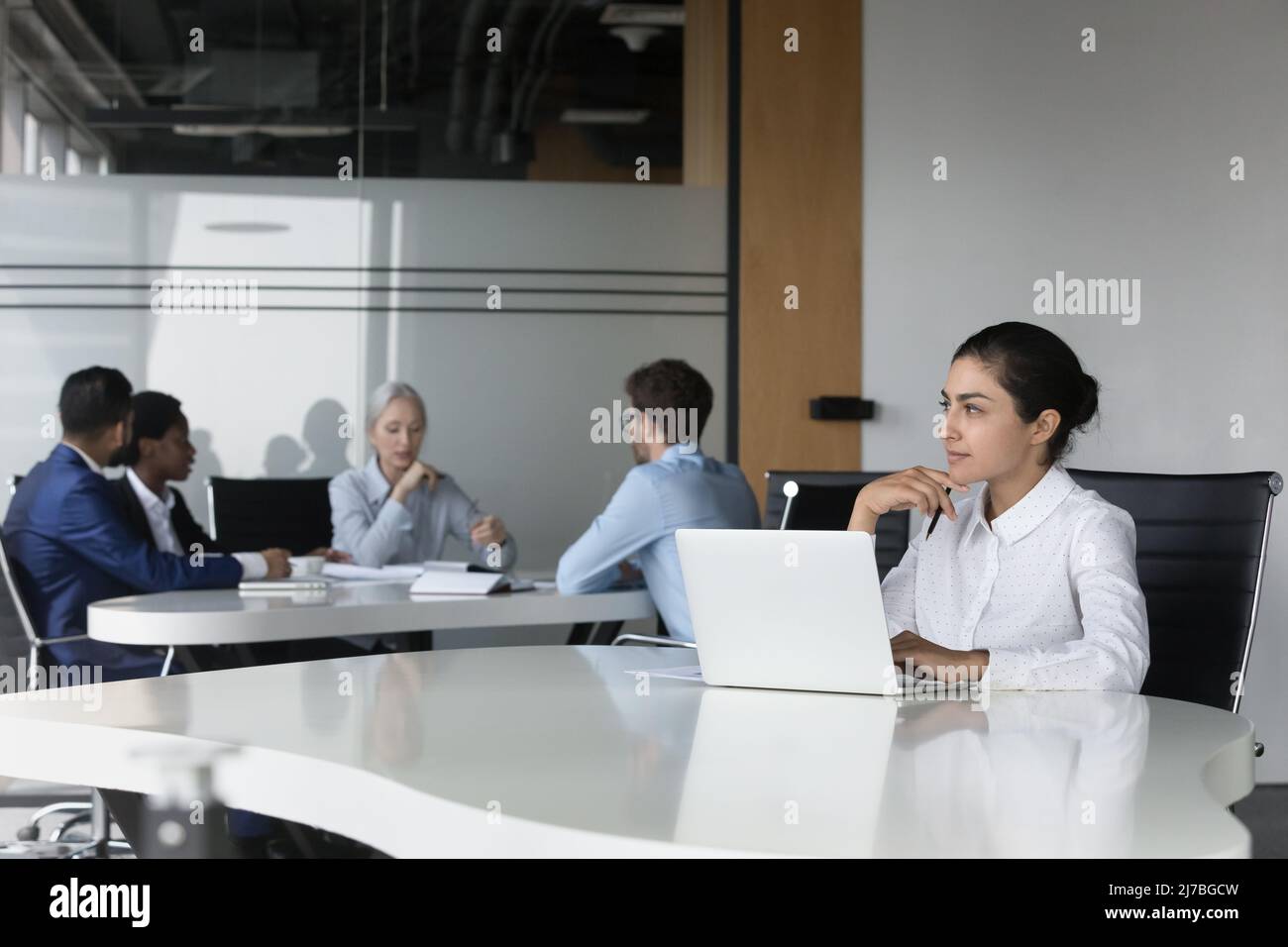 Thoughtful young Indian employee woman using laptop in co-working space Stock Photo