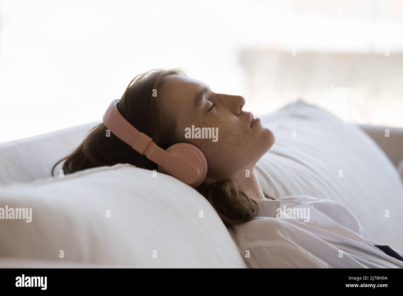 Serene sleepy teen girl in headphones resting on comfortable couch Stock Photo