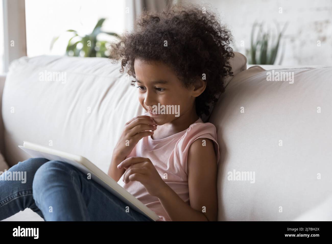 Curious African gen Z kid watching cartoon movie on tablet Stock Photo
