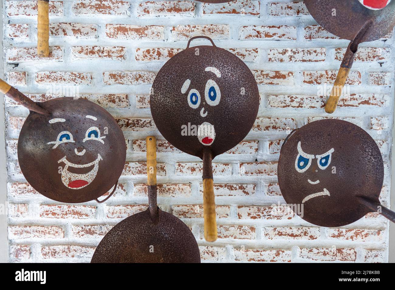 Old frying pans with painted faces, hang on a brick wall, close up Stock Photo