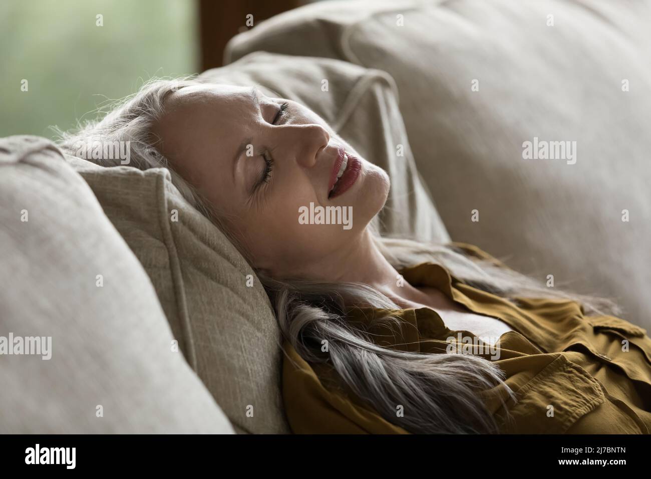 Calm lady resting with closed eyes on comfortable sofa Stock Photo