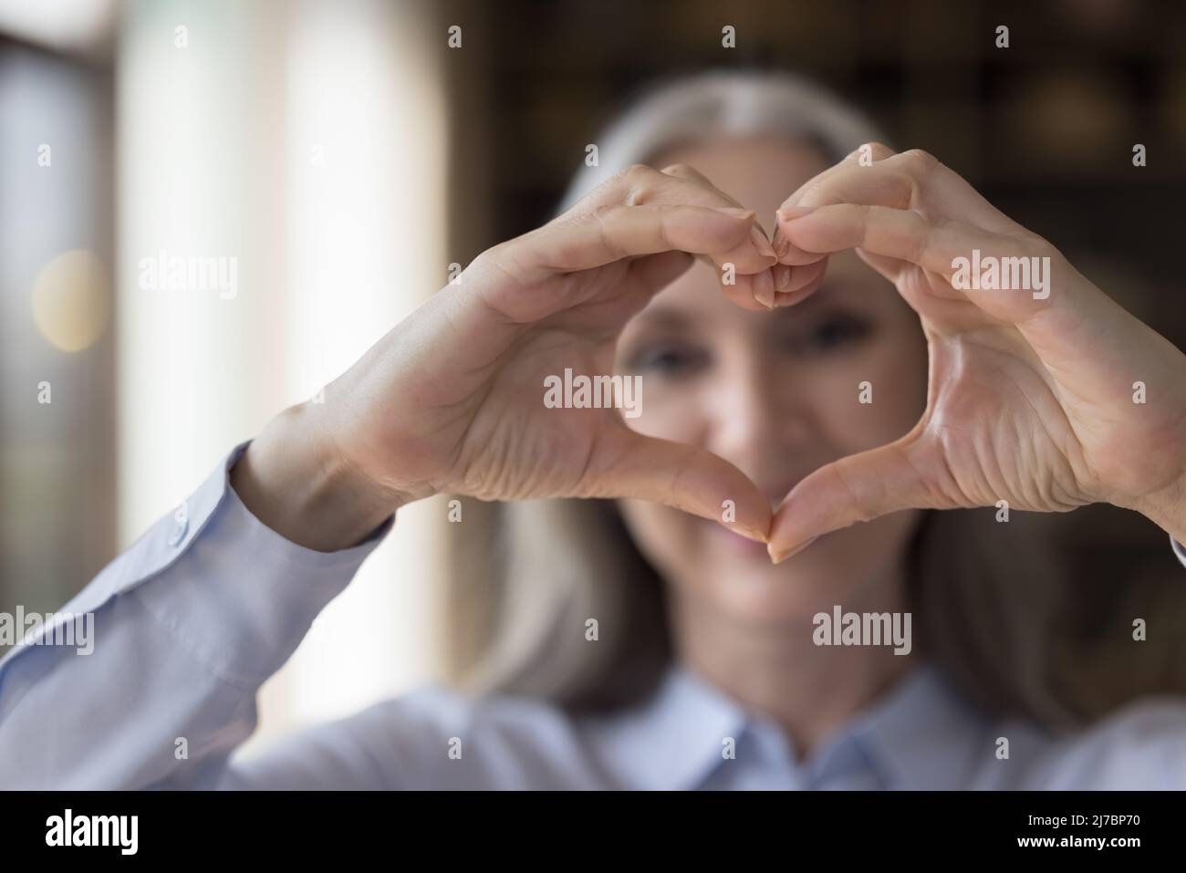 Senior woman showing finger heart shaped hands in focus Stock Photo