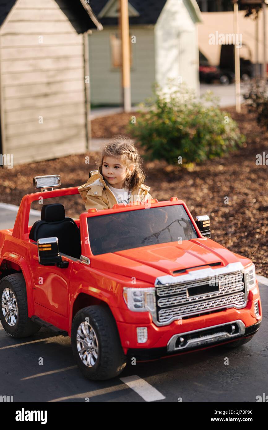 Cute little girl rides in a mini city on a red electric car jeep