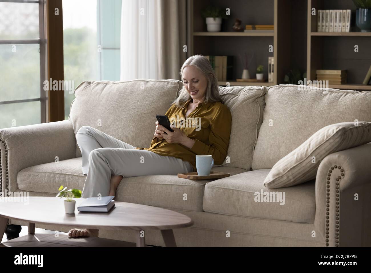 Cheerful grey haired lady using mobile phone at home Stock Photo