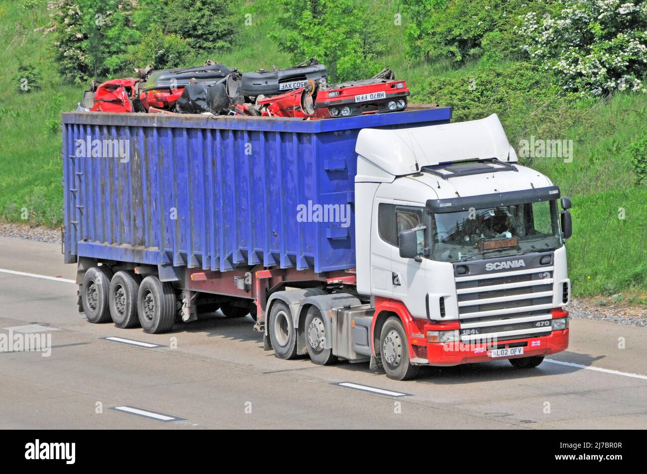 White unmarked hgv SCANIA lorry truck & blue articulated tipper trailer loaded with wrecked crushed scrap metal car bodies driving on UK motorway road Stock Photo