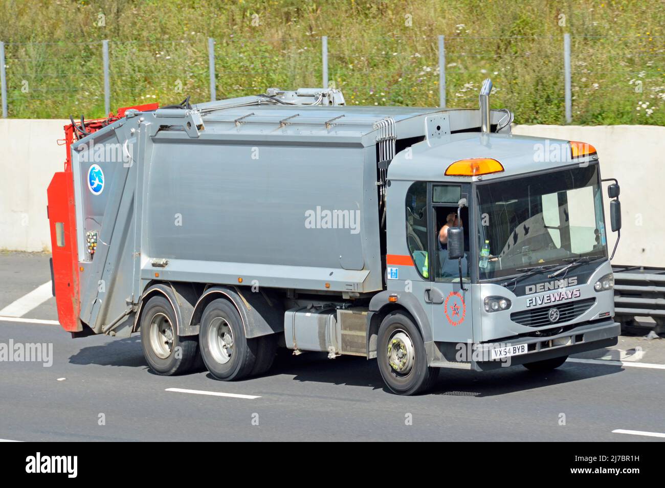 Driver in clean unmarked grey Dennis hgv bin lorry truck for collection of household & business waste rubbish garbage driving along UK motorway road Stock Photo