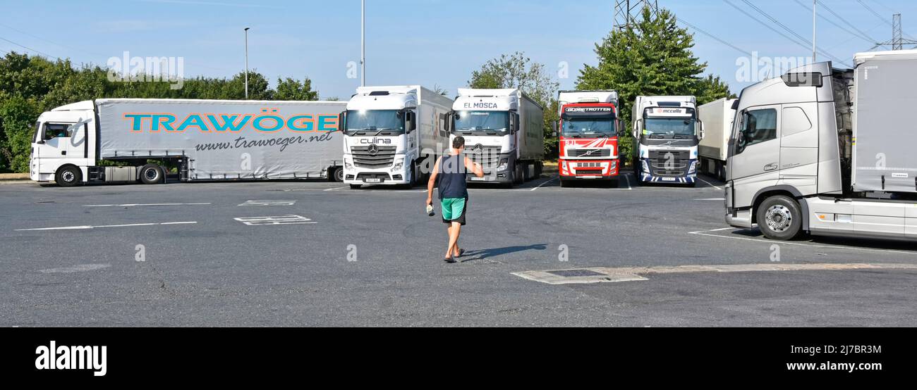 Lorry truck driver early morning walk back towards parked-up hgv articulated vehicles in overnight parking bays at motorway service station England UK Stock Photo