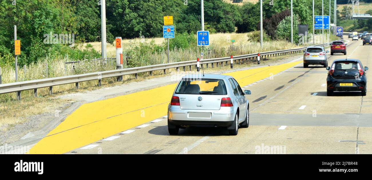UK yellow emergency refuge area & telephone layby on M25 smart motorway where regular hard shoulder becomes an extra traffic lane risky for breakdown Stock Photo
