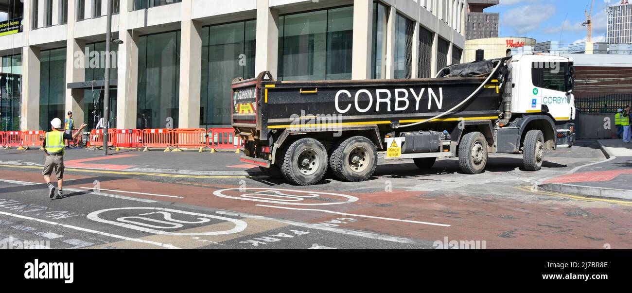 Side view of Corbyn groundwork & foundation business hgv tipper lorry truck reversing onto main road banksman stopping traffic East London England UK Stock Photo