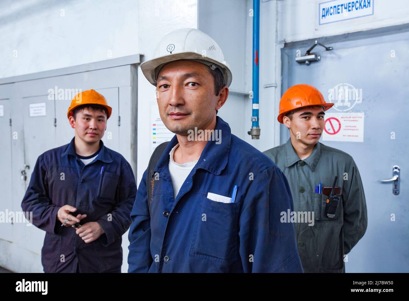Ust'-Kamenogorsk, Kazakhstan - May 31, 2012: Three Asian men, two workers and engineer (in center, white work helmet) on titanium metallurgy plant. Te Stock Photo