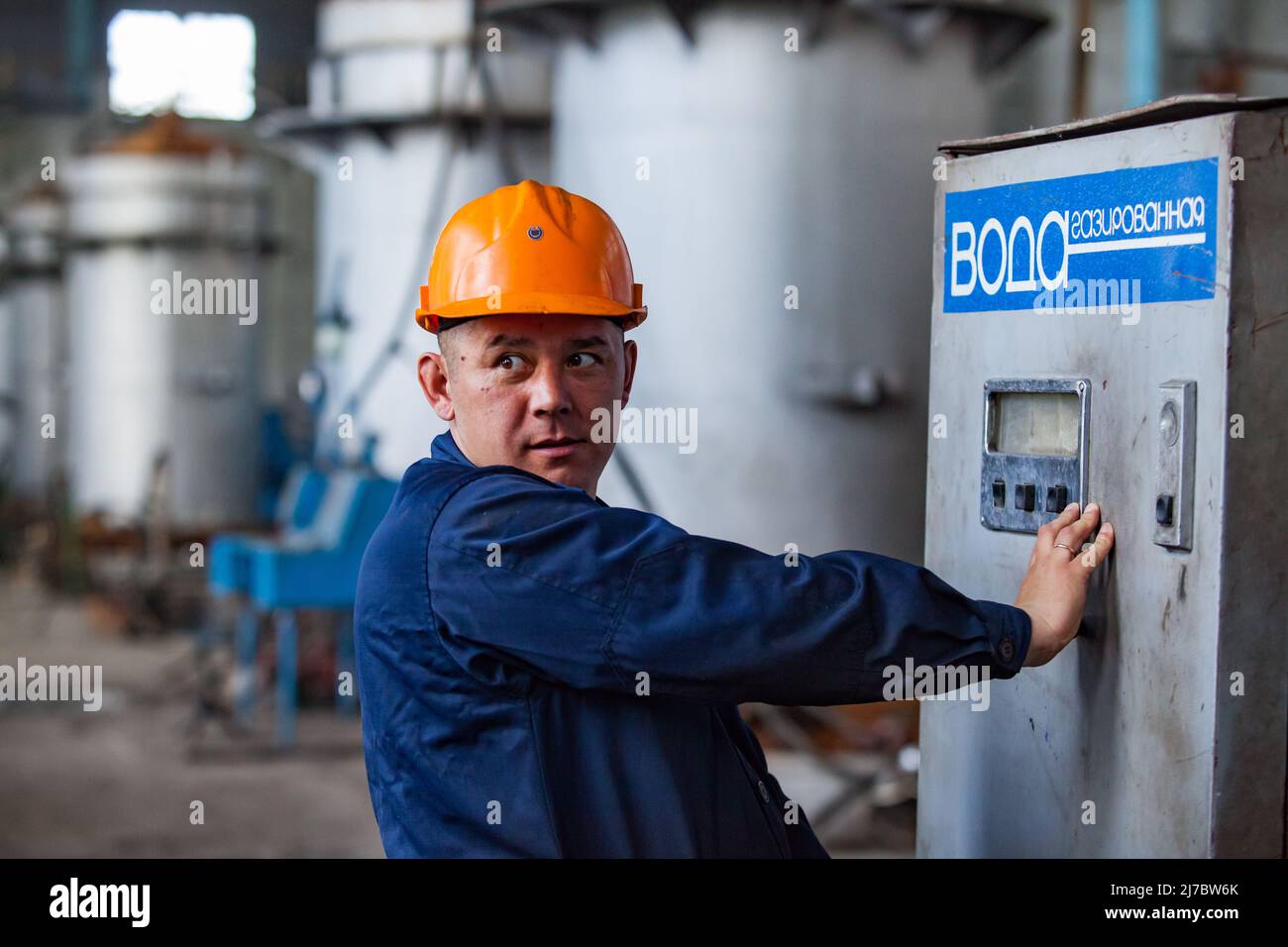Ust'-Kamenogorsk, Kazakhstan - May 31, 2012: Portrait of Asian worker man in orange hardhat in metallurgy factory workshop. Takes water from carbonate Stock Photo