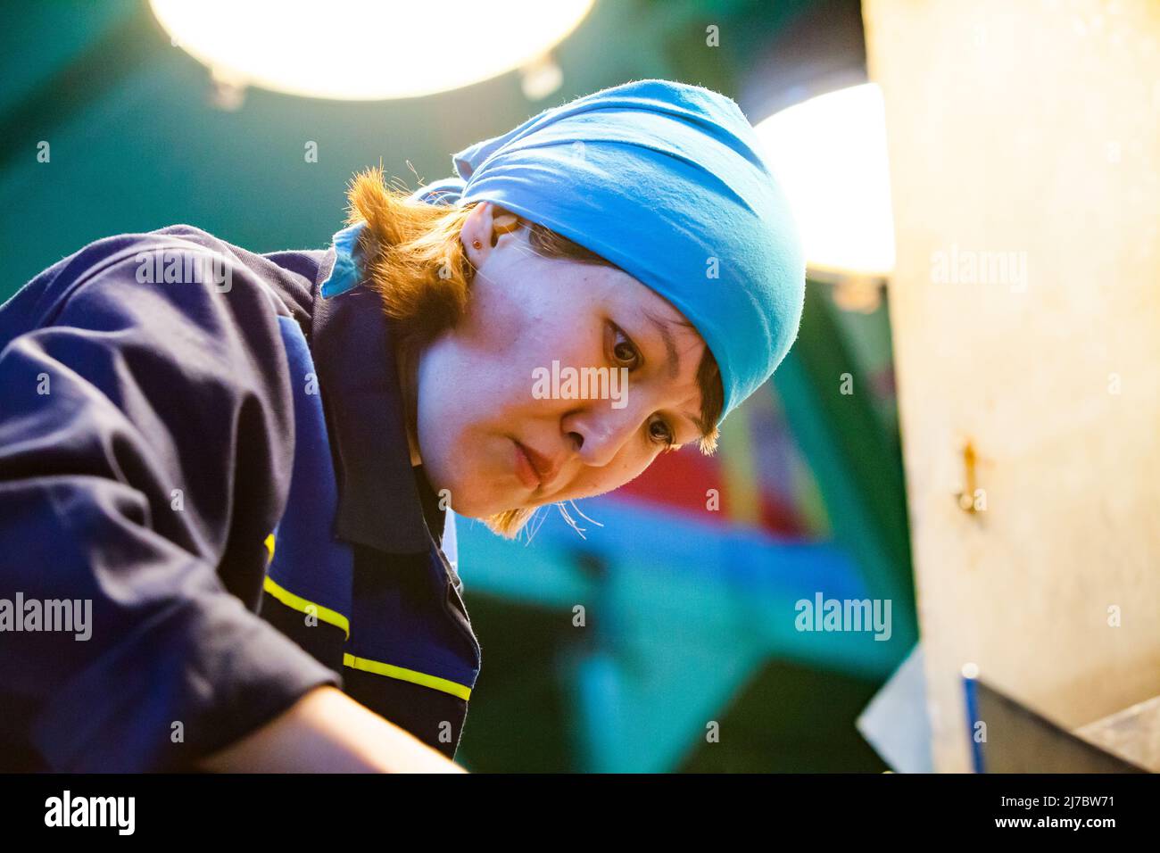 Ust'-Kamenogorsk, Kazakhstan - May 31, 2012: Portrait of young attractive Asian worker woman in blue bandana. Working on titanium ore conveyor. Stock Photo