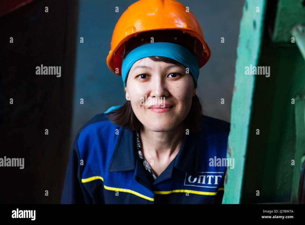 Ust'-Kamenogorsk, Kazakhstan - May 31, 2012: Portrait of young attractive Asian worker woman in blue bandana and orange hardhat. Looks straight in cam Stock Photo