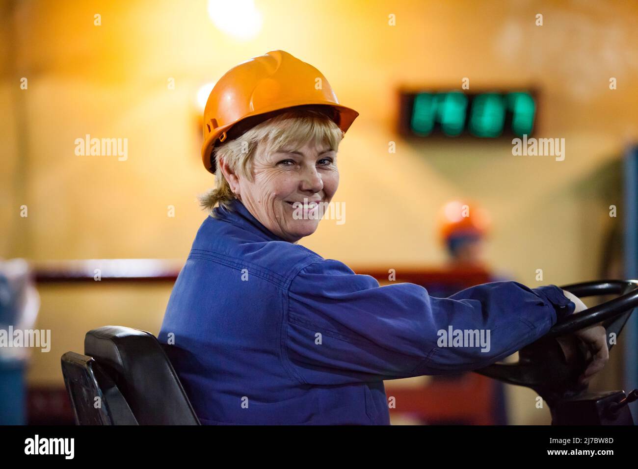Ust'-Kamenogorsk, Kazakhstan - May 31, 2012: Portrait of blonde woman worker in yellow hardhat smiling. Electric pallet stacker operator on warehouse. Stock Photo