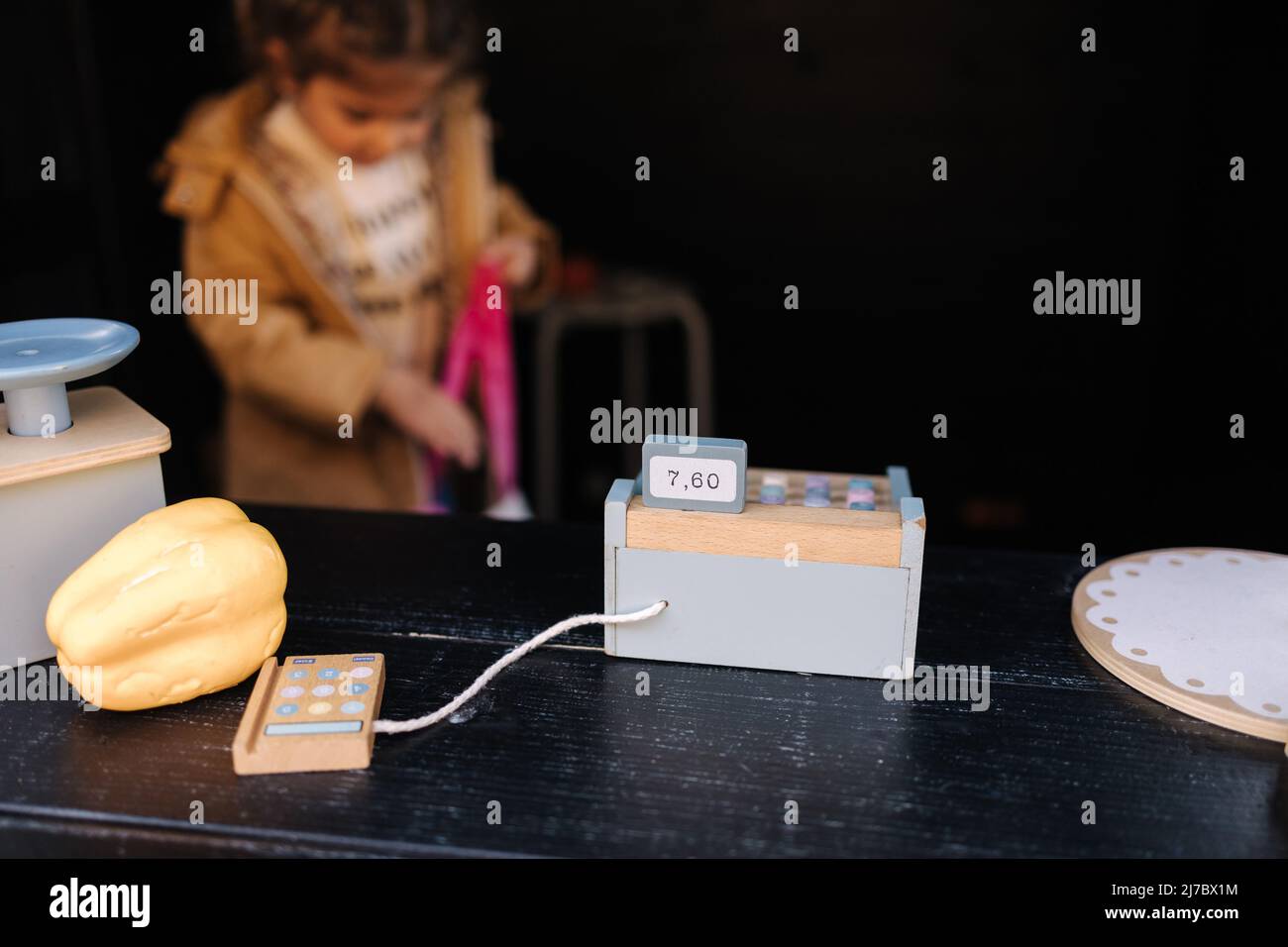 Adorable little girl sits inside of a toy market. Happy kid playing