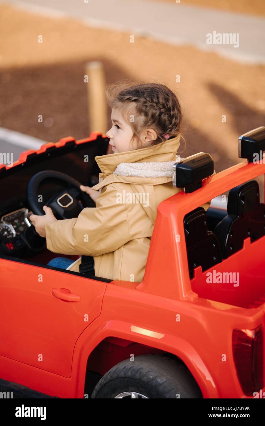 Cute little girl rides in a mini city on a red electric car jeep