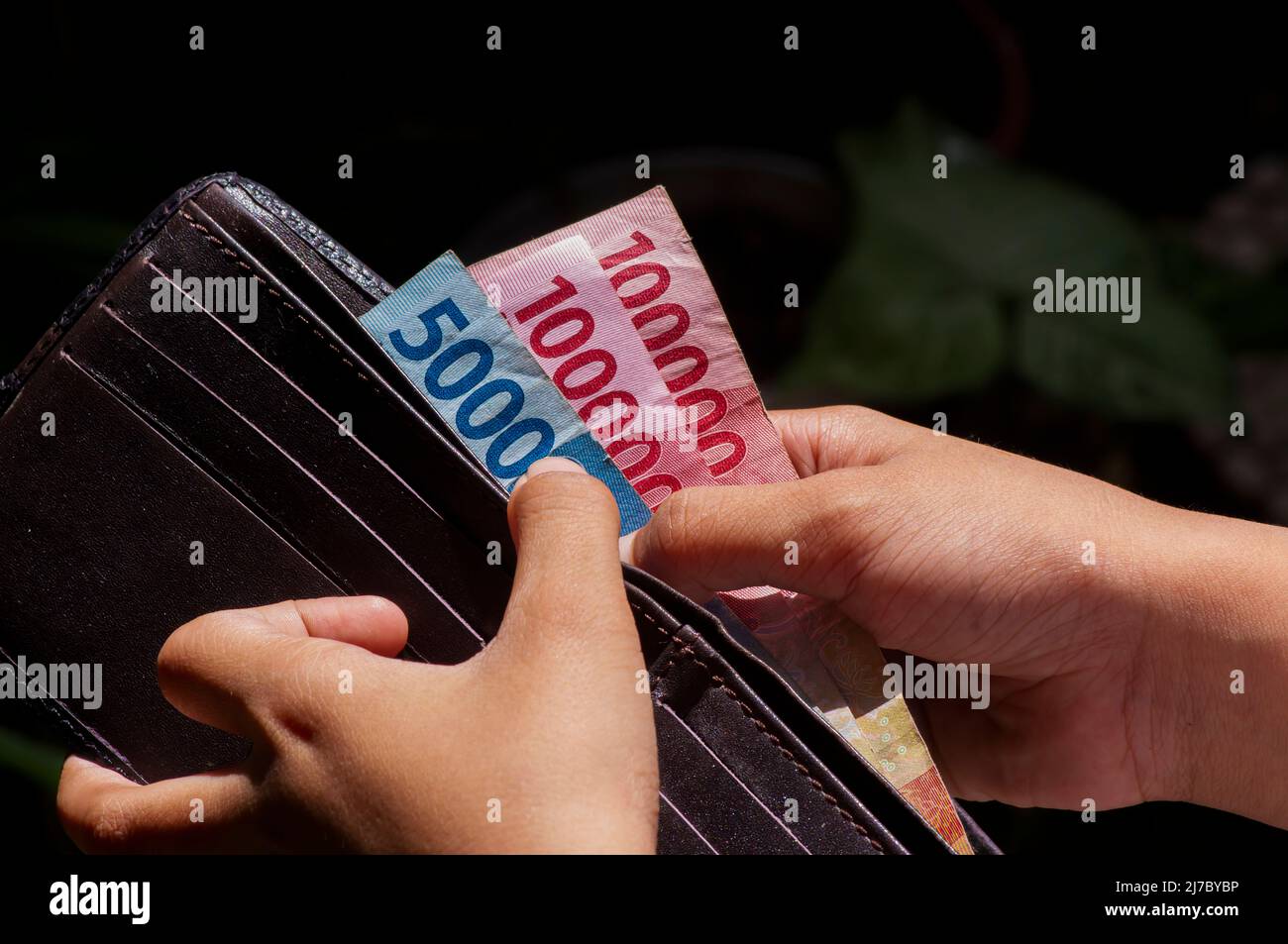 An Asian child take Indonesian money from wallet. Saving and giving concept Stock Photo