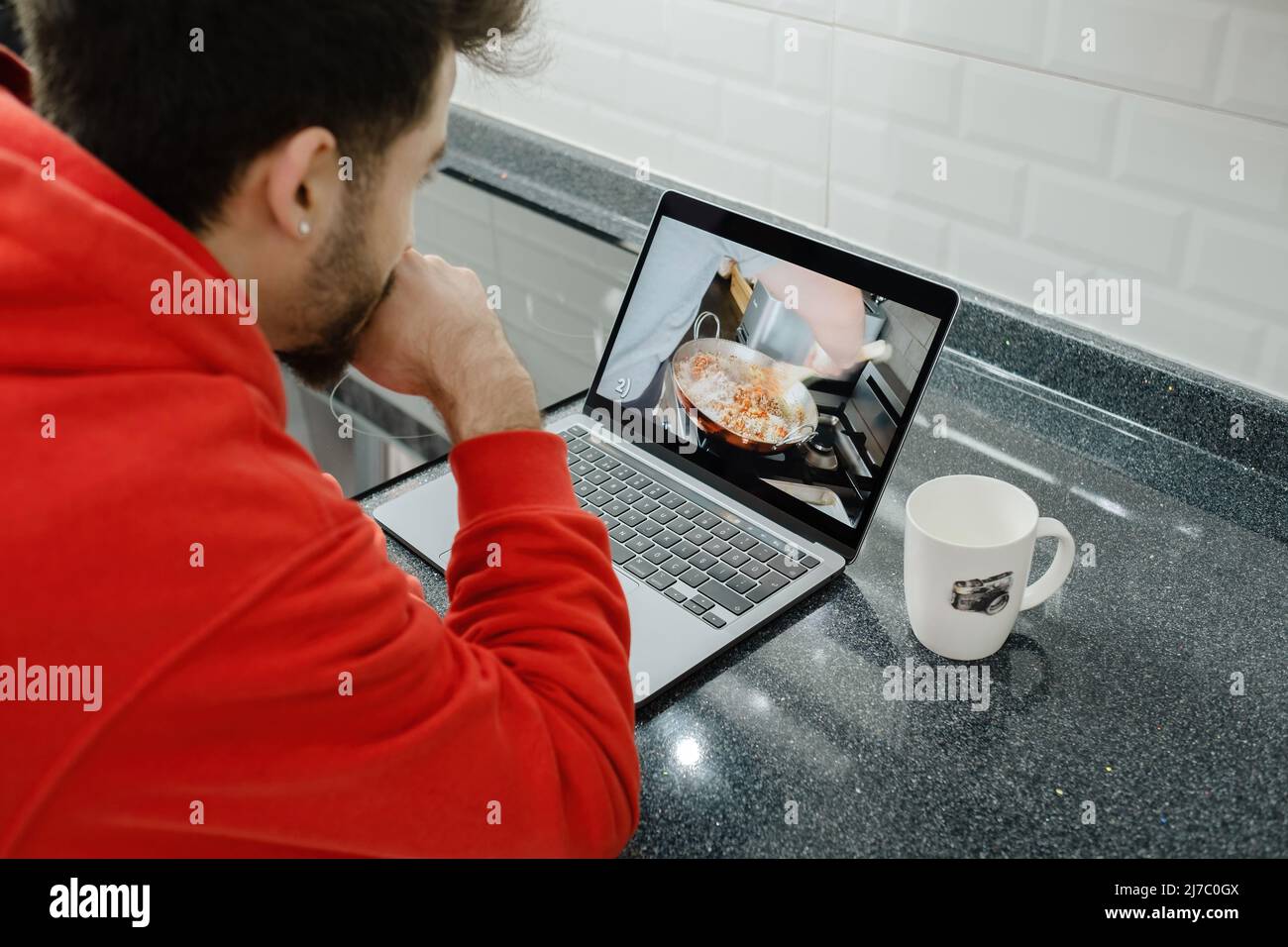 Recipe, young man is watching the steps to make tacos, black kitchen counter and laptop Stock Photo