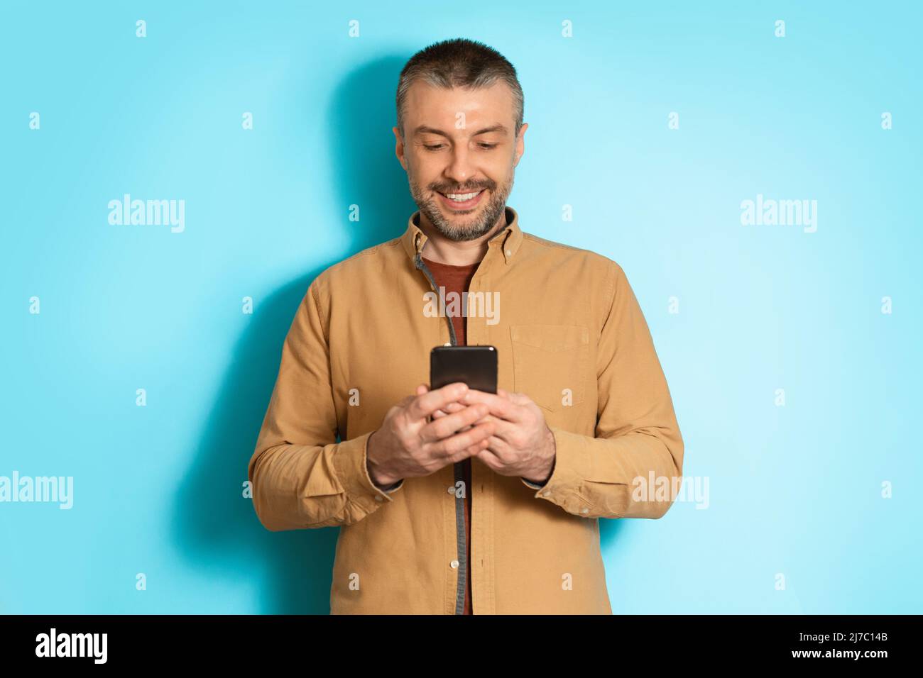 Cheerful Man Using Mobile Application On Cellphone Over Blue Background Stock Photo