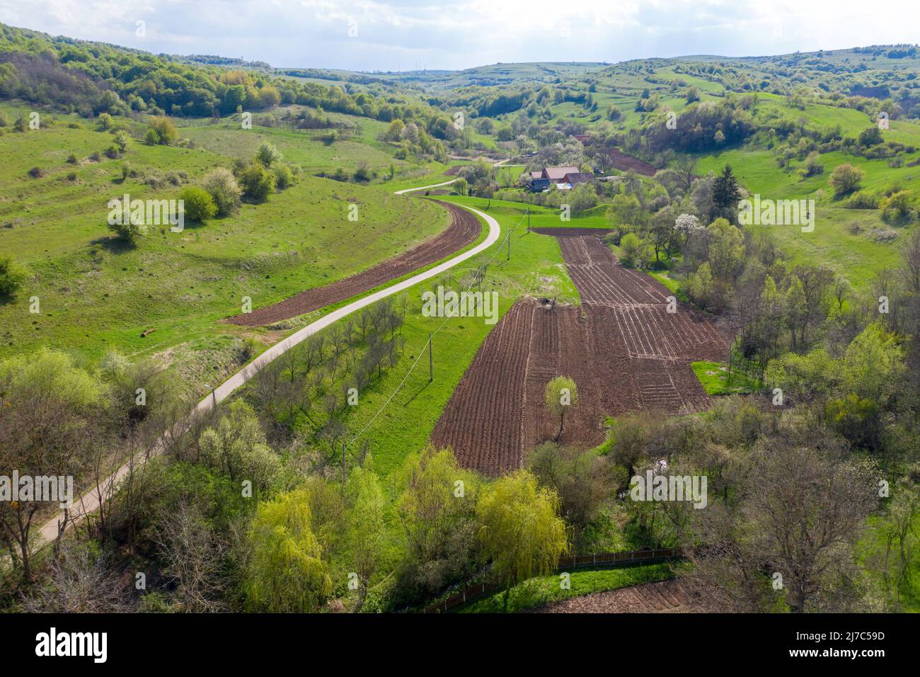 Aerial view of village road passing near an agricultural field. Spring view of green countryside hills Stock Photo