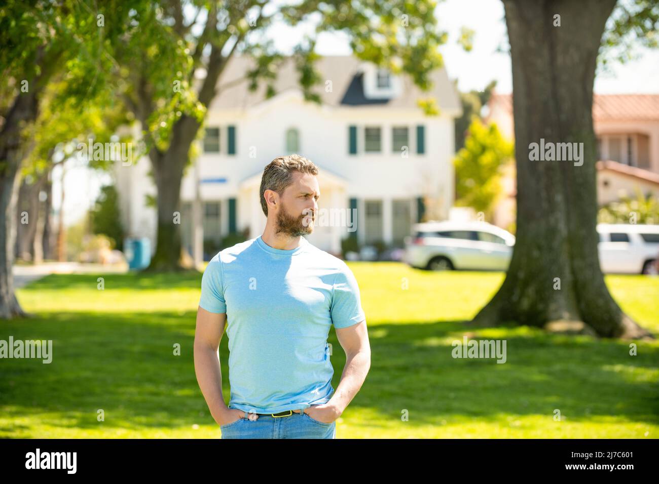 serious unshaven guy standing near new house, real estate Stock Photo