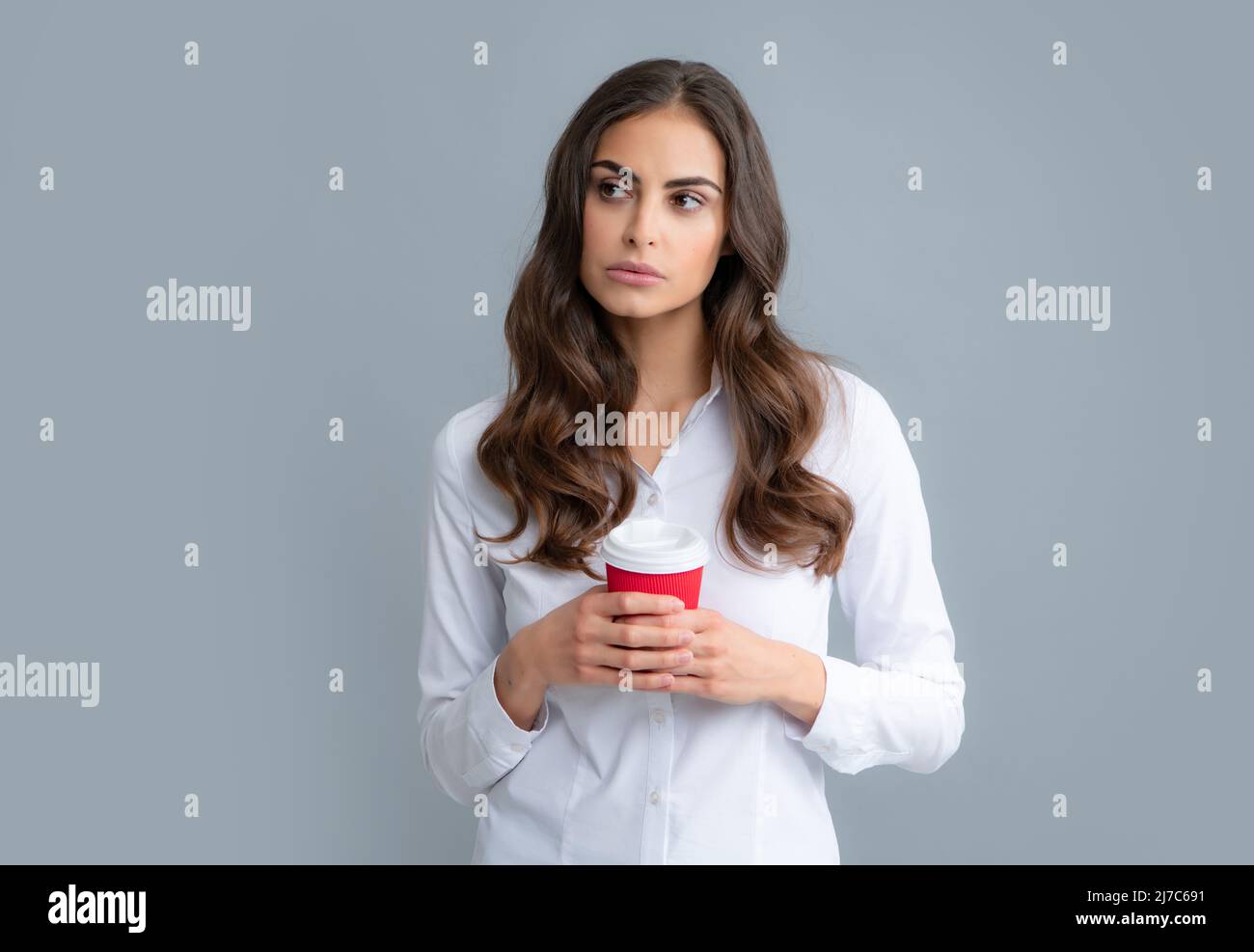 Portrait of nice cute girl holding cup of coffee. Young woman smiling with a coffee cup, isolated on gray background. Stock Photo