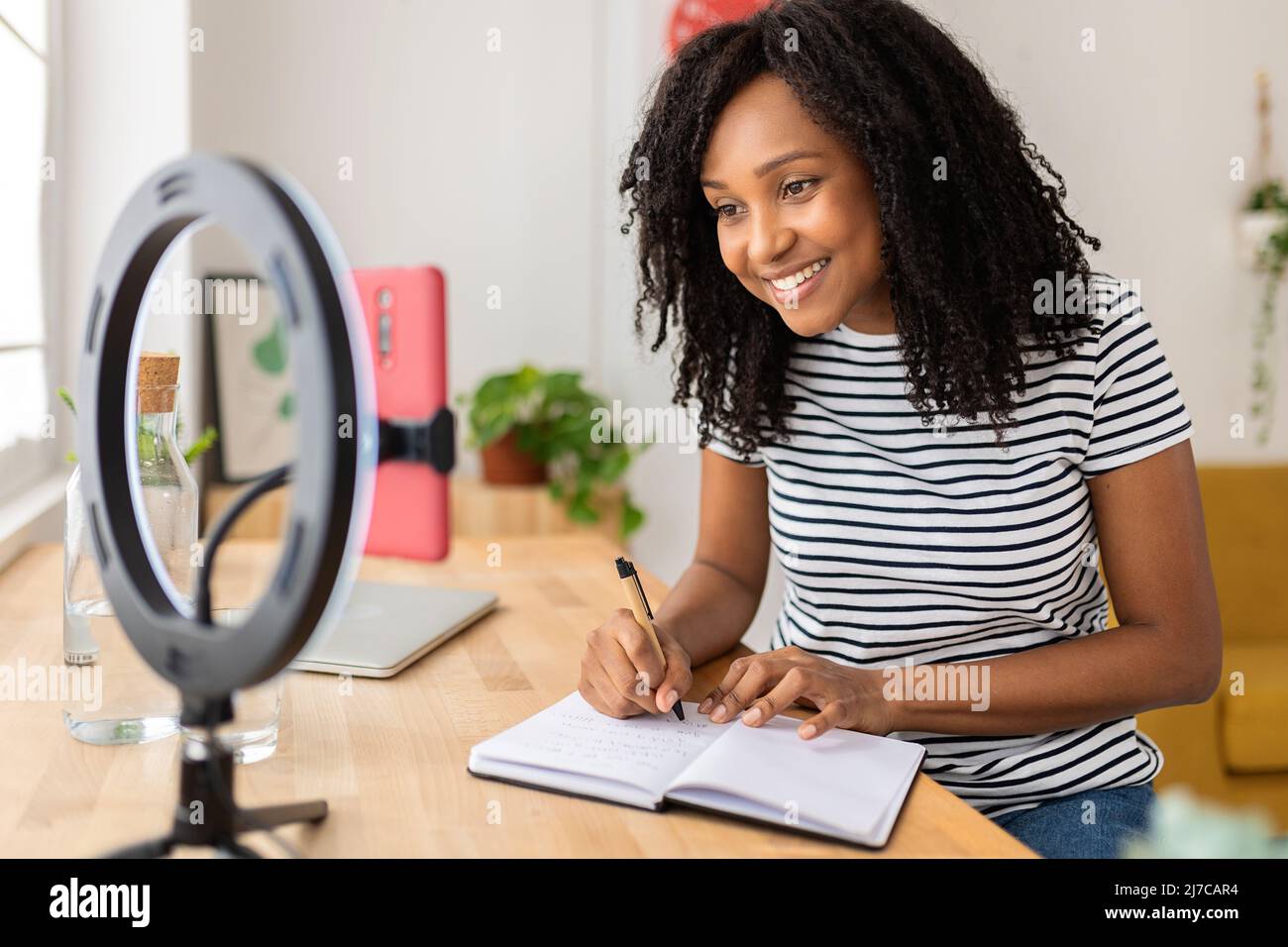 Young african american woman taking notes while watching video on mobile phone Stock Photo