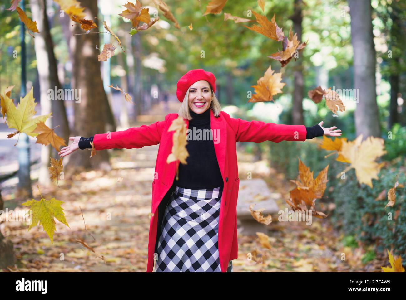 Cheerful woman throwing maple leaves in air Stock Photo