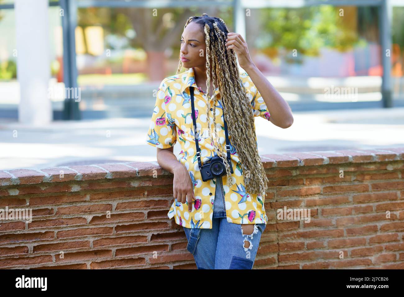 African influencer combed with colorful braids standing with a camera outdoors. Stock Photo