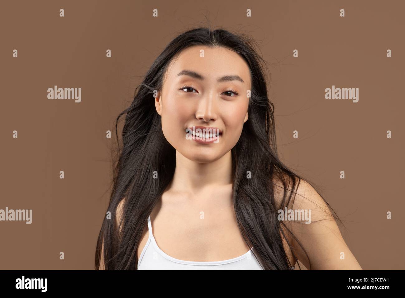 Natural beauty concept. Happy young asian lady with smooth perfect skin and silky hair posing over brown background Stock Photo
