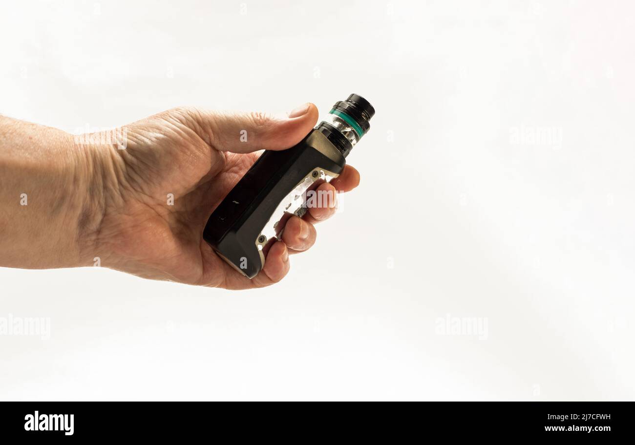elfbar elfa kaufen Hand holding vaping mod with tank filled with liquid. In background  footpath on meadow and hill with forest Stock Photo