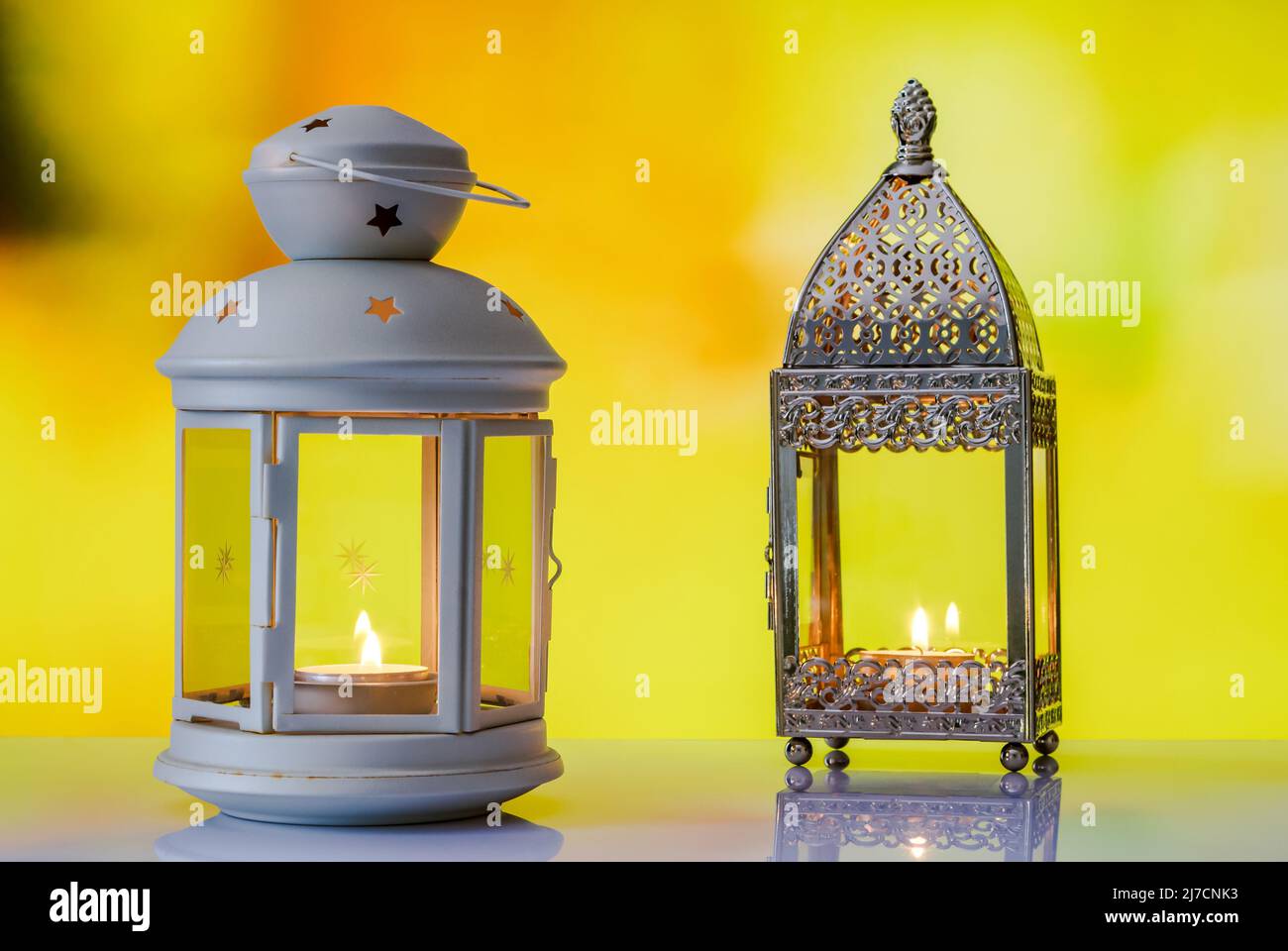 two stylish lanterns with candles burning inside on a blurred soft