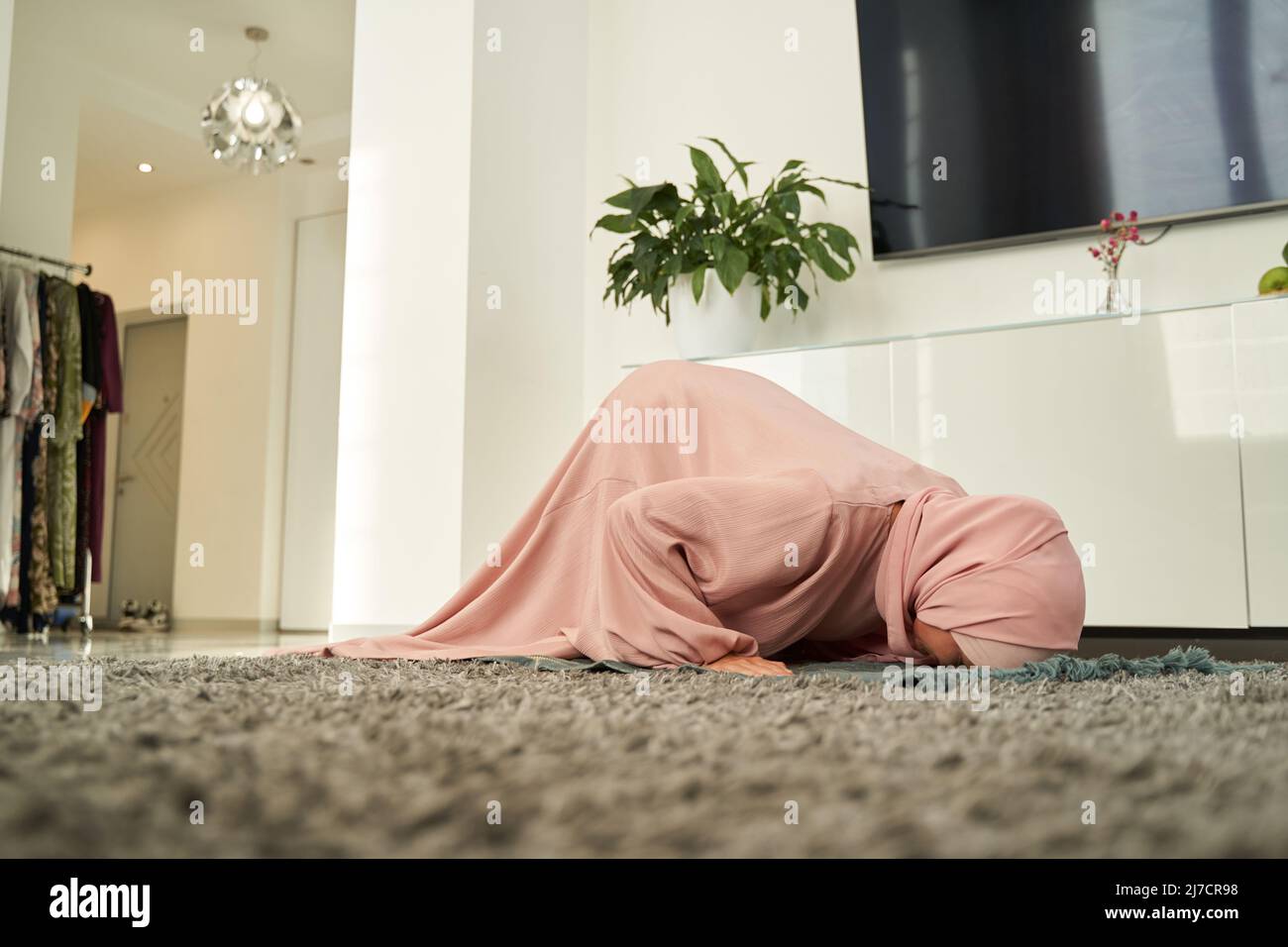 Muslim woman bowing down on praying carpet at home Stock Photo