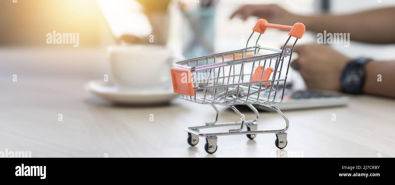 shopping cart on table with hand of people on laptop background Stock Photo