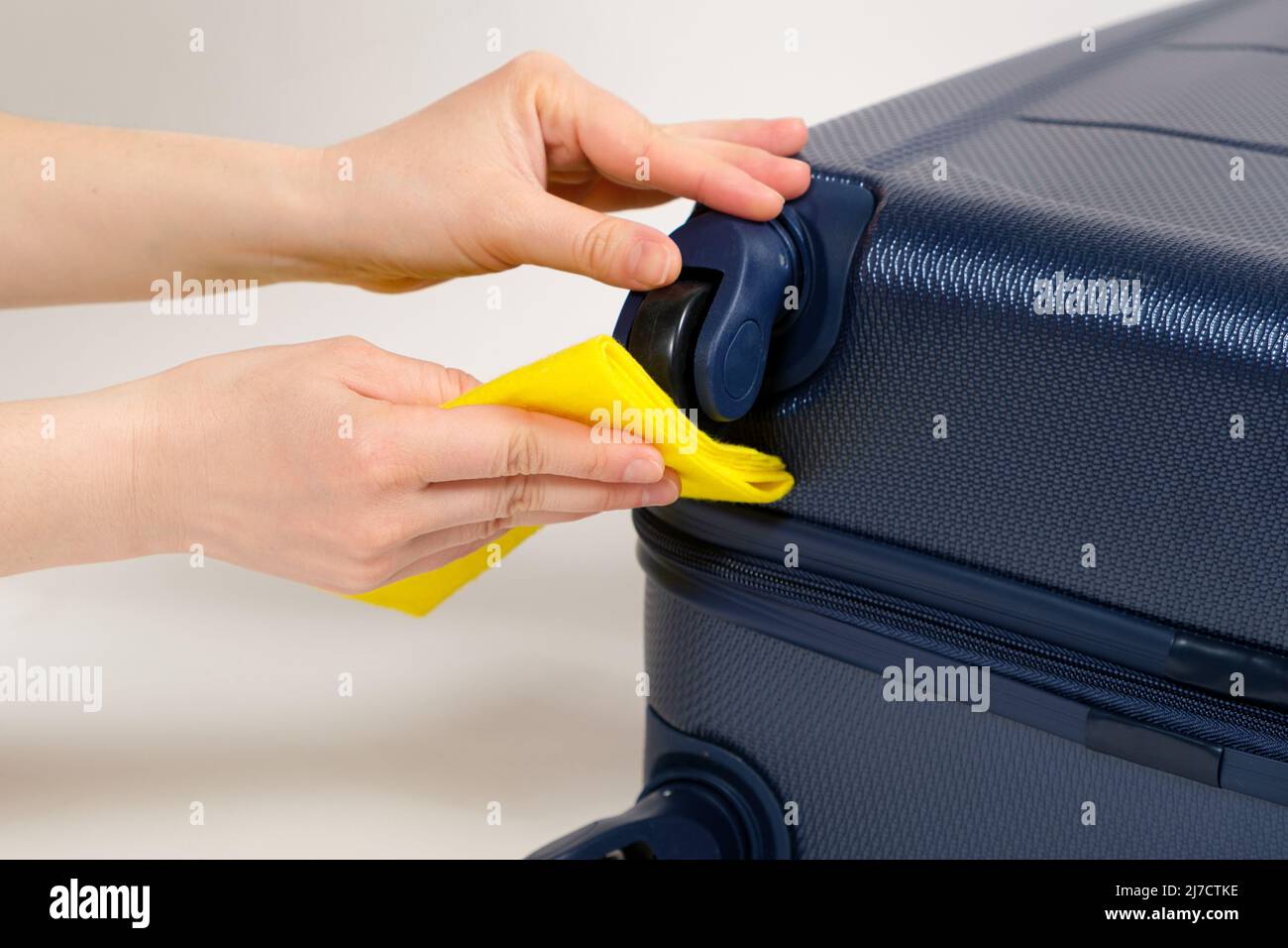 Cleaning the rubber wheels of a travel suitcase with a yellow rag from