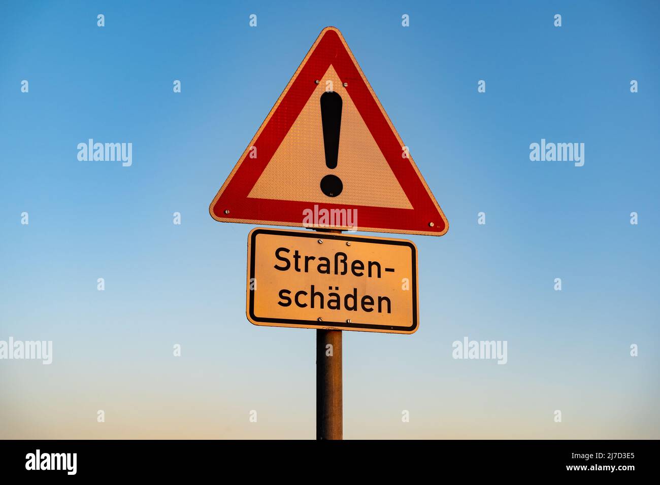 Road sign with a warning against road damages. In German language it says 'Straßenschäden' which should slow down the traffic because of a bumpy road. Stock Photo