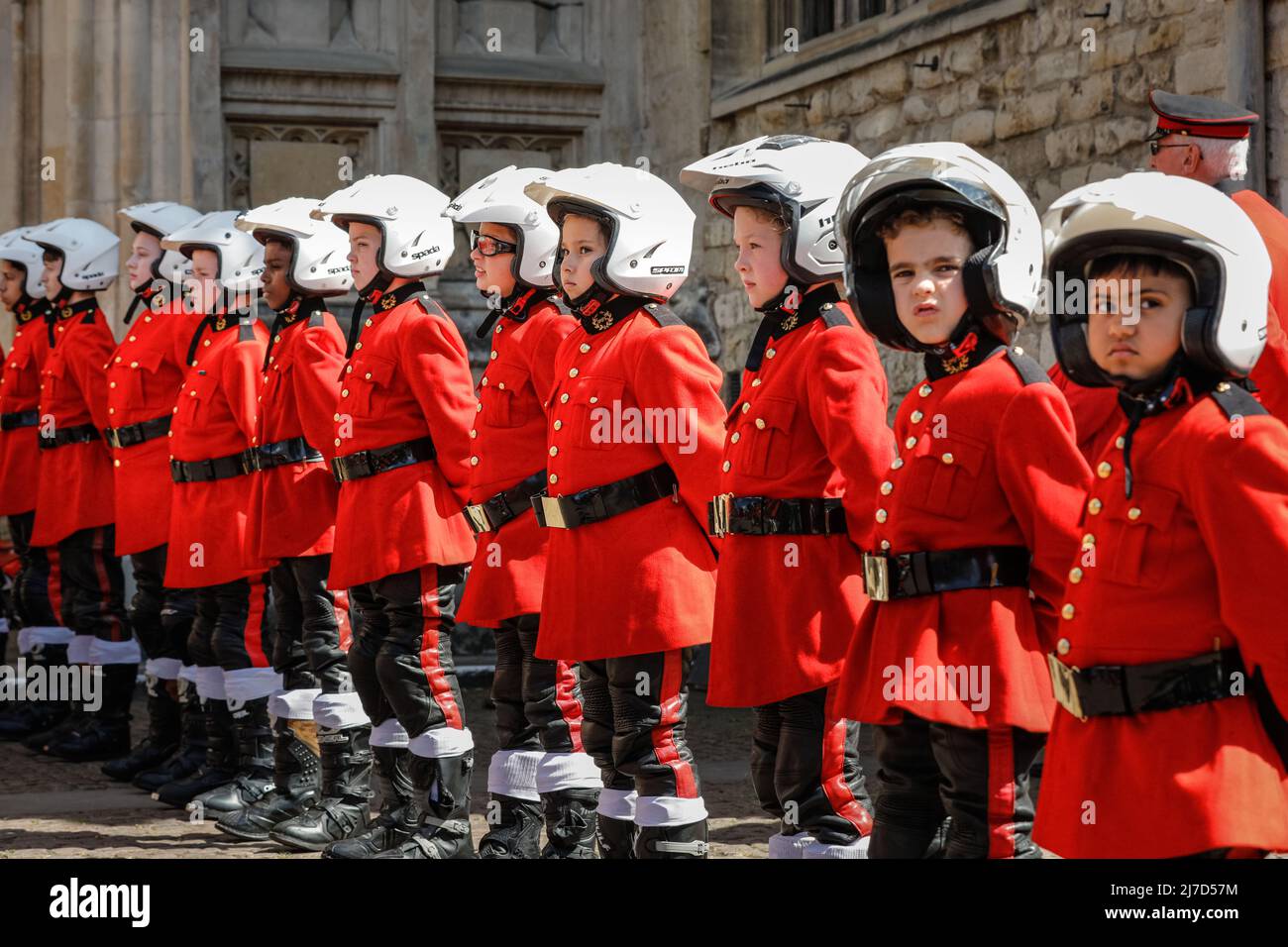 London, UK, 8th May 2022. Children in colourful red 'biker' uniforms and helmet line the entrance of Westminster Abbey whilst members of the club enter for an evensong service and blessing of bikes. The 59 Motorcycle Club was founded by the Reverend John Oates as a youth club at the Eton Mission, Hackney Wick and later grew from Ace Cafe in London in 1962, is celebrating its 60th birthday with a church service at Westminster Abbey in Westminster today. Many of the clubs members have arrived on their bikes, riding under the Stewardship of Father Sergiy Diduk. Stock Photo