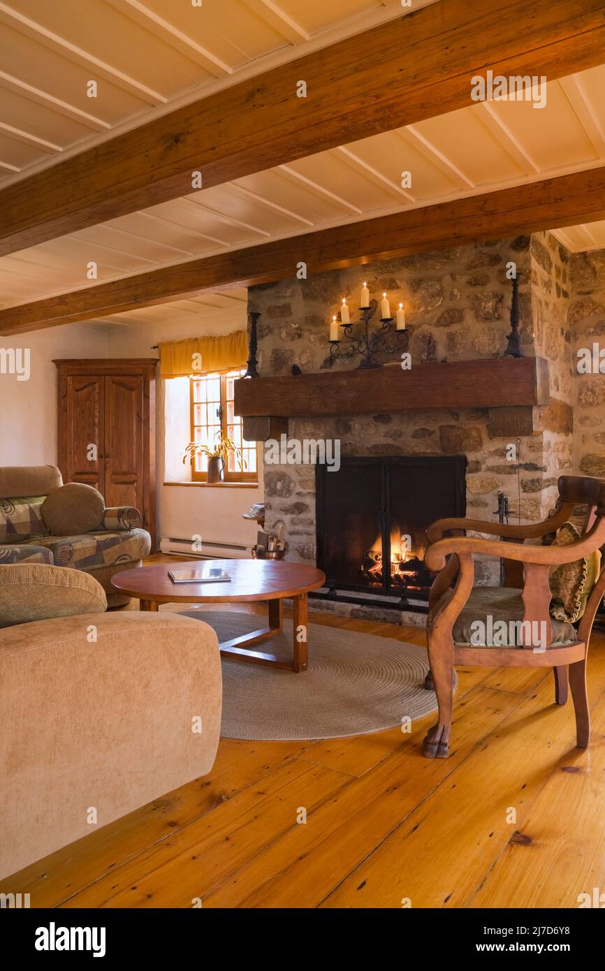 Lit stone fireplace and antique furnishings in living room inside 1800s log home. Stock Photo