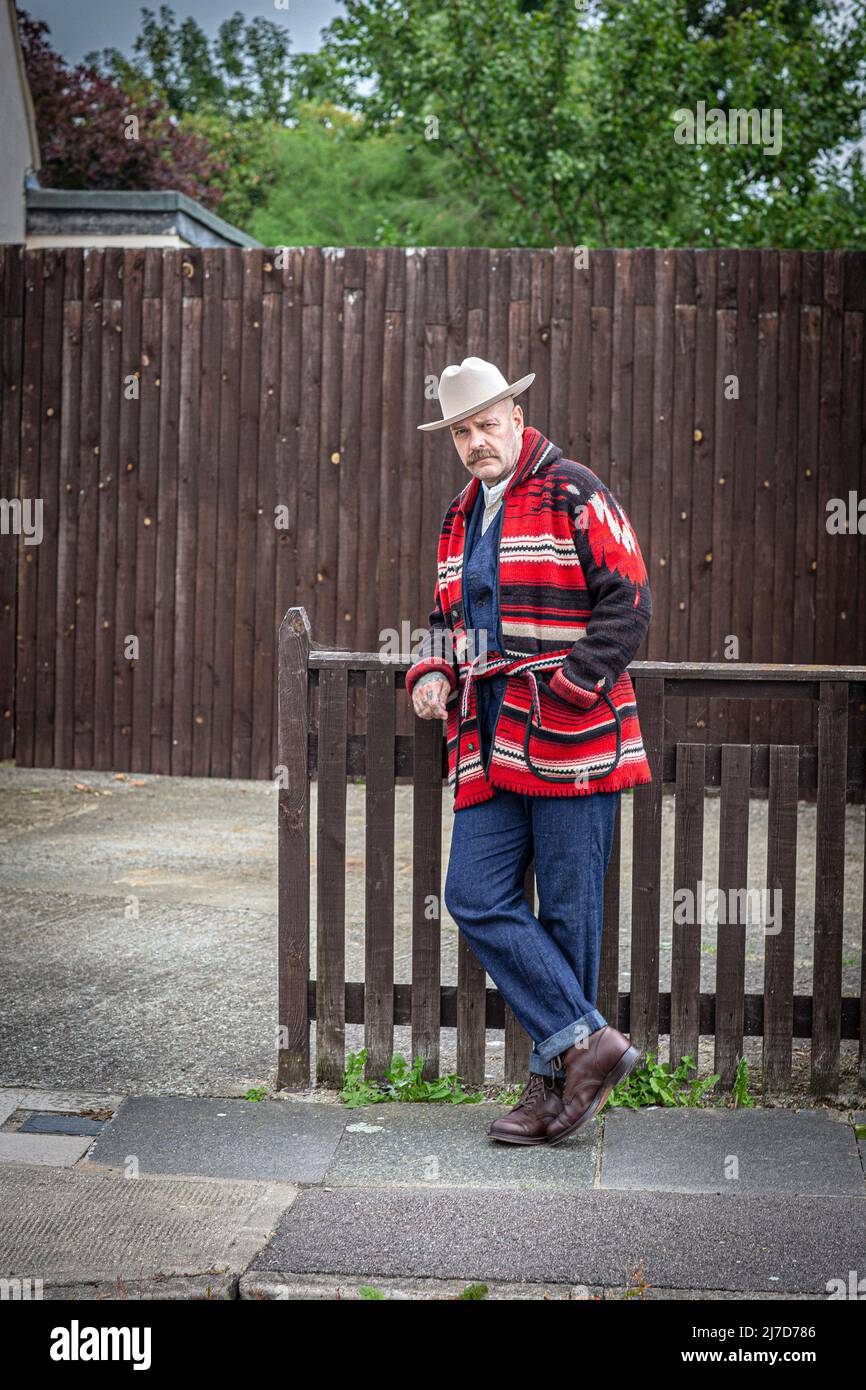 A man wearring western wear and hat standing in front of wooden fence. Stock Photo