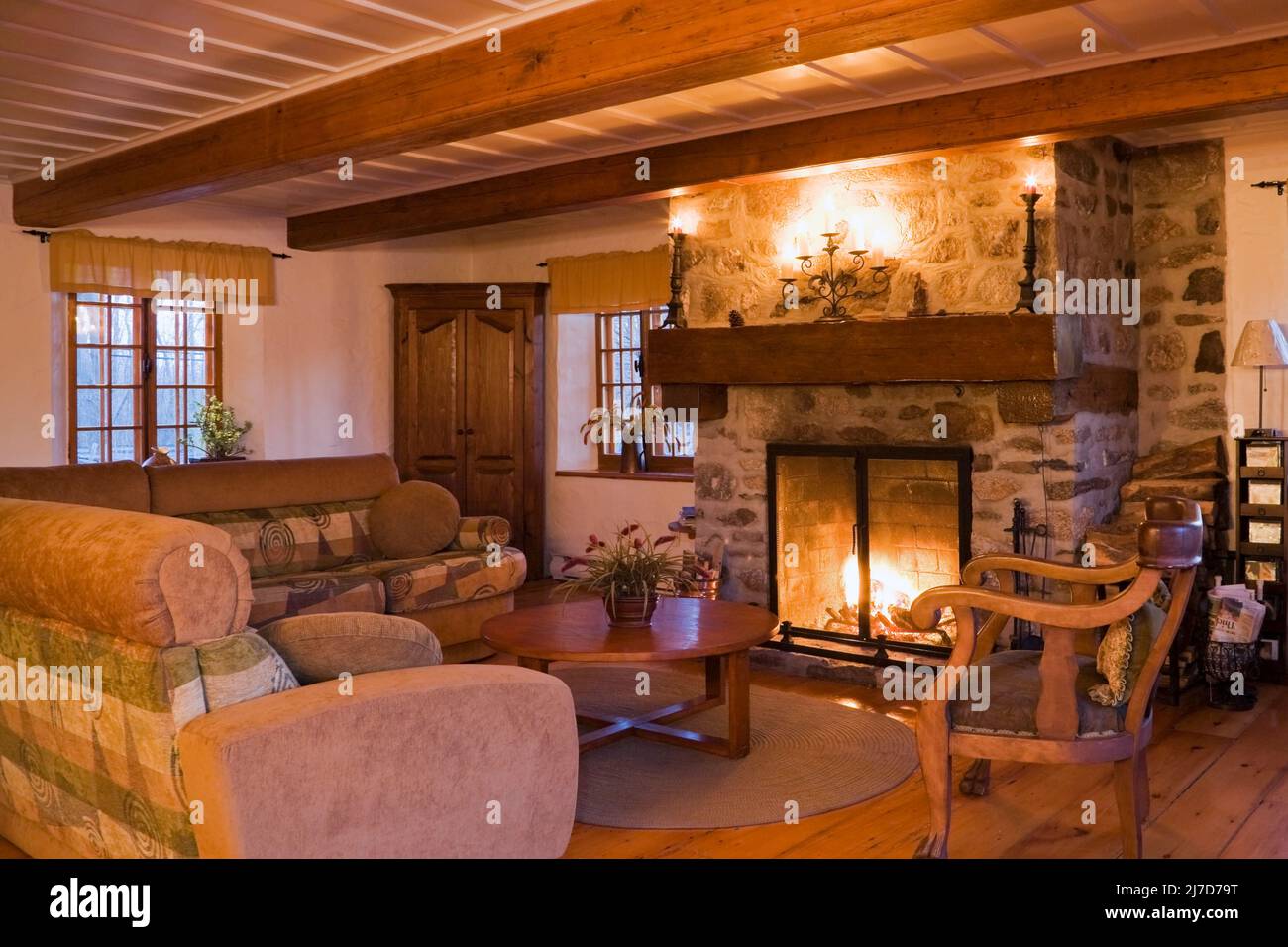 Lit stone fireplace and antique furnishings in living room inside 1800s log home. Stock Photo